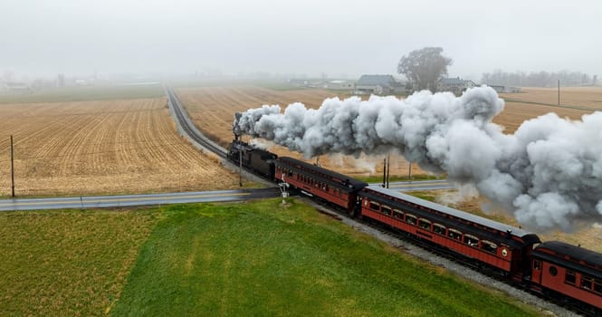 A vintage steam train travels through a foggy countryside, billowing clouds of smoke against golden fields. The scene captures the essence of rural life in a tranquil autumn setting.