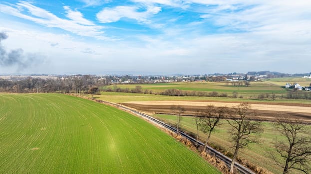 A sweeping view of lush green fields stretches out towards the horizon with scattered towns visible. The sky is partly cloudy, hinting at a peaceful day in a rural setting.