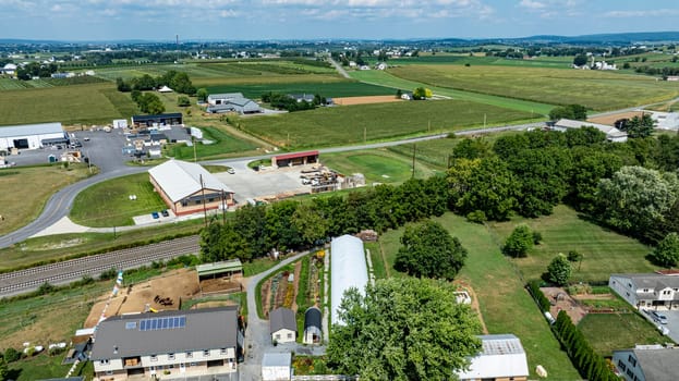 This aerial perspective captures a vast rural landscape featuring multiple farms, green fields, and winding roads under a clear blue sky. The scene highlights the serenity of countryside life.