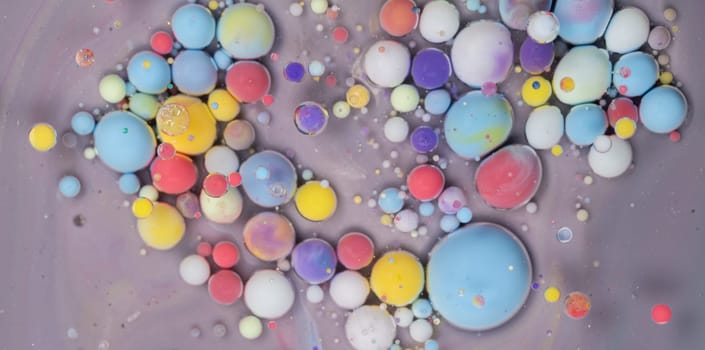 An intricate display of colorful spheres in various sizes floats on a smooth gray surface, demonstrating a captivating mix of paint and liquid. The arrangement creates an artistic abstract effect.