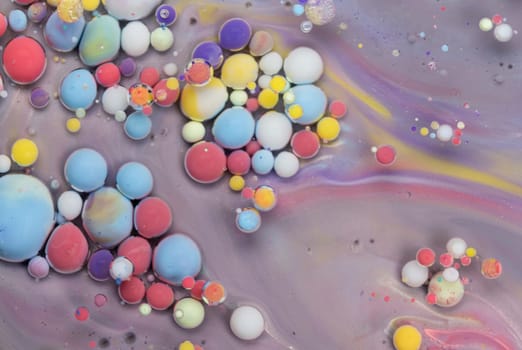 Tiny droplets of vibrant colors float in swirling patterns against a pastel background, creating an abstract, mesmerizing visual effect that captivates the eye.