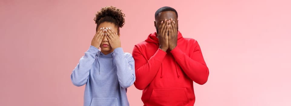 Two african-american man woman standing pink background hide faces close eyes palms tired looking lies upset waiting sign command see, playing hide-n-seek, unwilling spot personal problems.