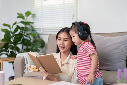 A mother and daughter experience a story together, with the daughter focused on listening while wearing headphones at home, enhancing their mother daughter connection.
