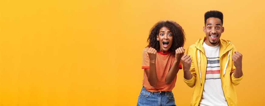 Two friends cheering and supporting mate on competition yelling joyfully clenching fists in supportive geture smiling broadly waiting with amazement and excitement for win and victory. Lifestyle.