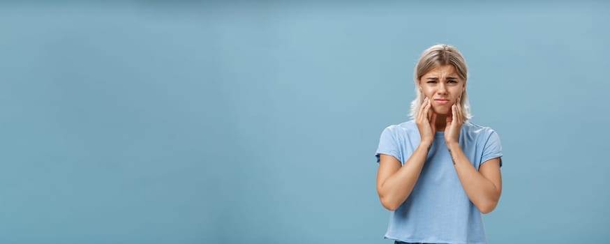 Girl feeling pain in teeth after drinking hot coffee. Displeased unhappy troubled young girl with blond hair frowning feeling discomfort in mouth holding hands on cheeks suffering toothache.