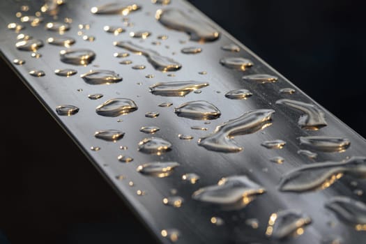 Detail of Water droplets caused by rain perched on the metallic surface. Rain water drops on a stainless steel handle, Natural Pattern of dew drops or raindrops on silver metal background for wallpaper poster and banner design, Selective focus.