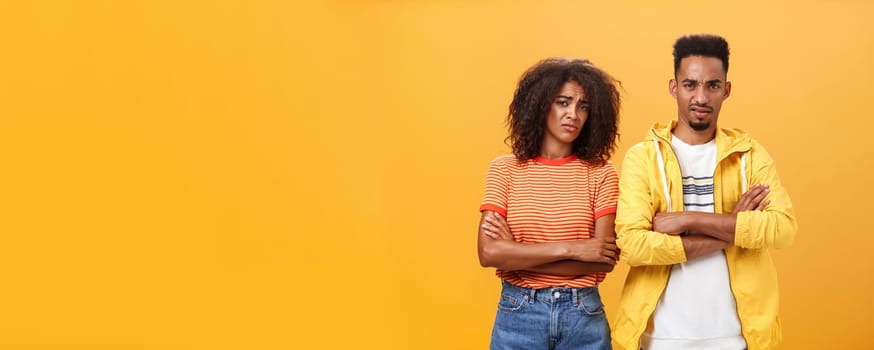 Two friends dislike lame idea of mate. Portrait of dissatisfied unimpressed african american man and woman crossing arms on chest in aversion frowning doubtful and disappointed over orange wall.