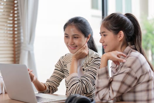 Two female students share a moment of enjoyment while studying together on a laptop, highlighting digital learning and engagement.