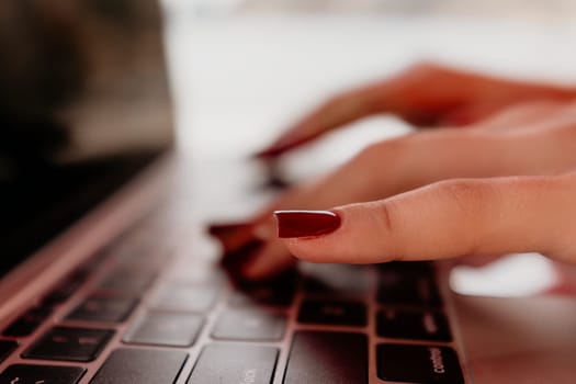 Close-up of hands with red nail polish typing on a laptop keyboard.