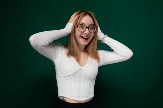 A woman with glasses is standing and wearing a white top. She has a thoughtful expression on her face as she looks ahead.