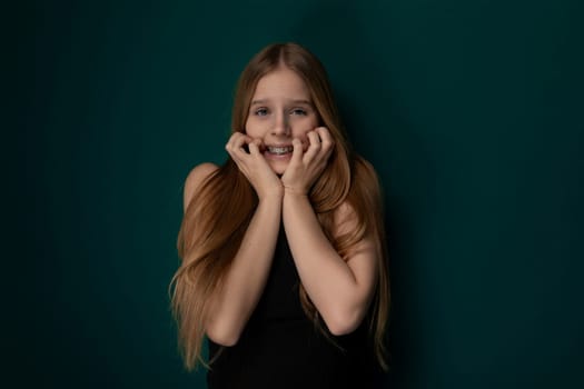 A girl with long red hair stands confidently in a pose for a photograph. She looks directly at the camera, showcasing her striking features and vibrant hair color.
