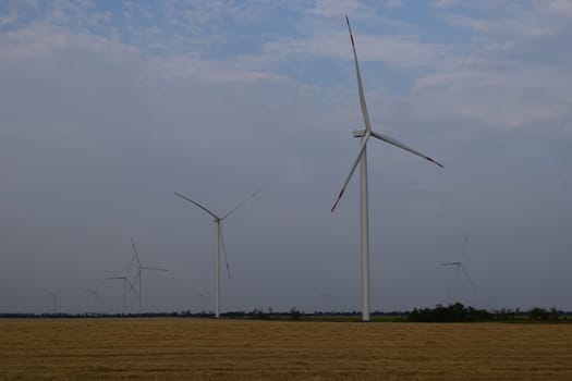A field of windmills spin in front of a colorful evening sky. A wind turbine is used to produce electricity. Wind energy is the use of wind for electrical power. It's a sustainable, renewable energy