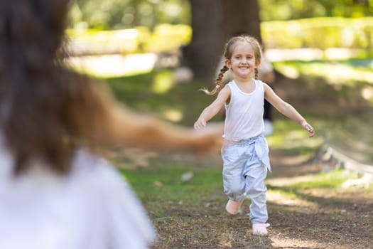 Happy little girl running through the park to her mother with open arms on a sunny summer day