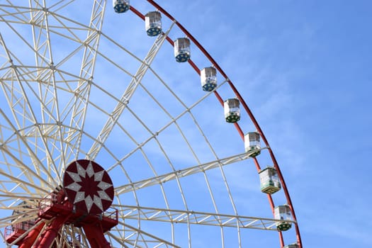 Ferris wheel against the blue sky in the city park with copy space. Part of a white metal construction of the attraction Ferris wheel with observation cabs high against the blue sky with white clouds