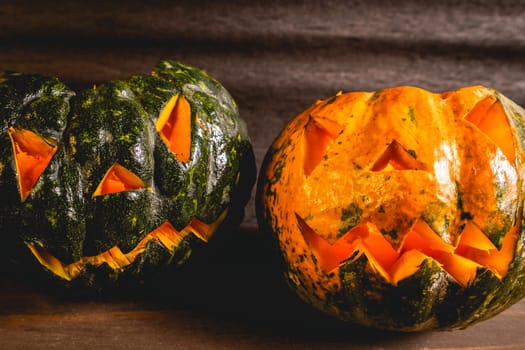 Two small pumpkins carved for Halloween. On a dark background.
