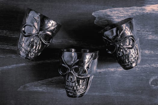 A couple of shot glasses in the shape of a skull, for a Halloween Party. On a wooden background, in black and white.