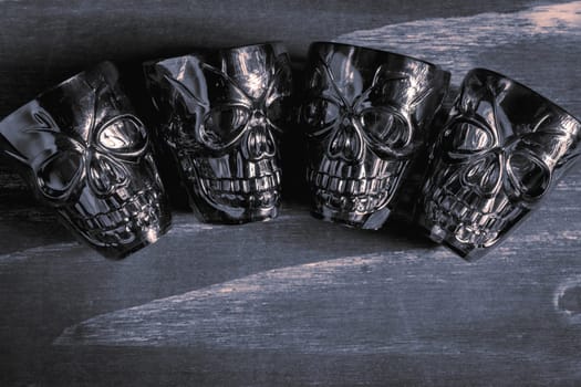 A couple of shot glasses in the shape of a skull, for a Halloween Party. On a wooden background, in black and white.