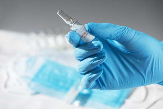 Coronavirus vaccine concept: covid-19 vaccine in hand with blue protective gloves.