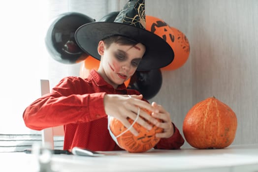 Teen boy in costume drawing coronavirus image on the pumpkin for the Halloween celebration. Halloween carnival with new reality with pandemic concept.