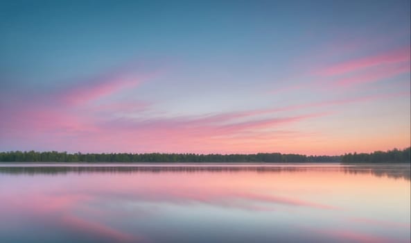 A calm body of water reflects a beautiful sky with pastel pink and blue clouds. The sunset is casting a warm glow over the water. There are trees in the distance along the shoreline, which are slightly obscured by the soft light.