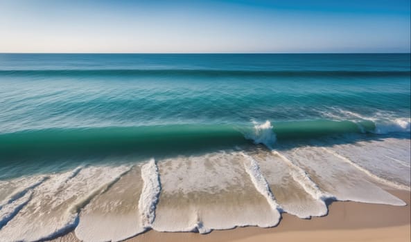 The image shows a large wave breaking on a sandy beach. The water is a clear blue and the sand is white. The sky is clear and blue.