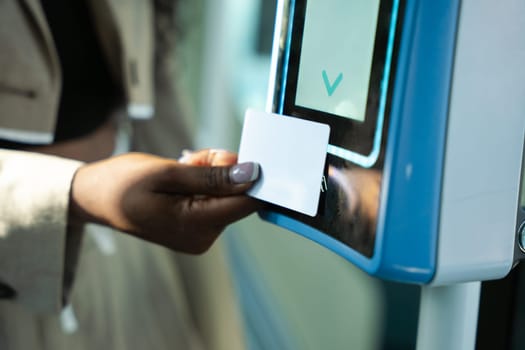 Young African American woman standing in front of a cashier, paying for her transportation ticket with her card, to access a bus station.