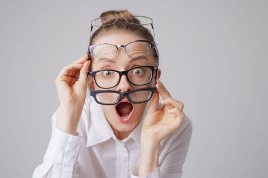 Surprised woman in several pairs of glasses with shocked expression on white background, astigmatism concept