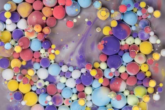 Bright and colorful droplets of paint float on a surface, forming abstract patterns. The composition features an array of sizes and colors, showcasing artistic creativity.