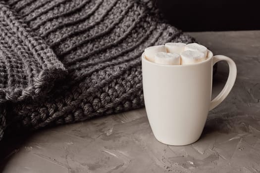 Creating a warm atmosphere with a cup of hot cocoa, marshmallows, and a cozy grey knitted blanket for relaxation