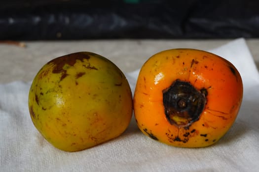 The image shows two round, orange persimmon fruits stacked on a white paper towel.