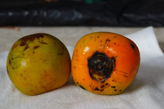 The image shows two round, orange persimmon fruits stacked on a white paper towel.