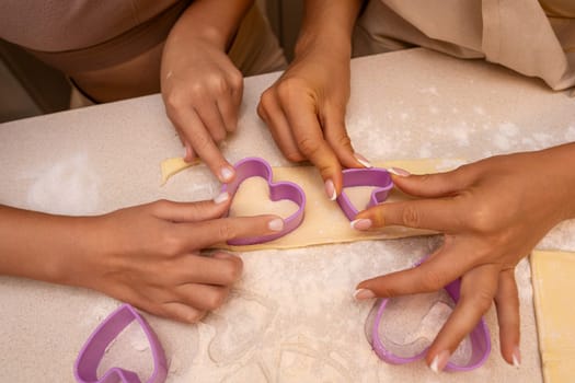 Two people are using heart-shaped cookie cutters to cut out cookies from dough on a table.