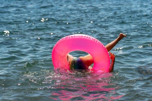 A child in a pink floatie has fallen into the water. They are submerged with only their legs and the floatie visible.
