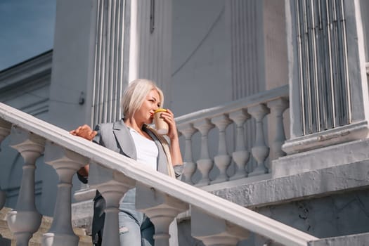 A woman is standing on a white staircase with a cup in her hand. She is smiling and looking up at the sky