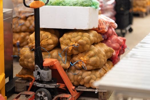 Killograms of potatoes in mesh bags on a trolley at the market. Mid shot