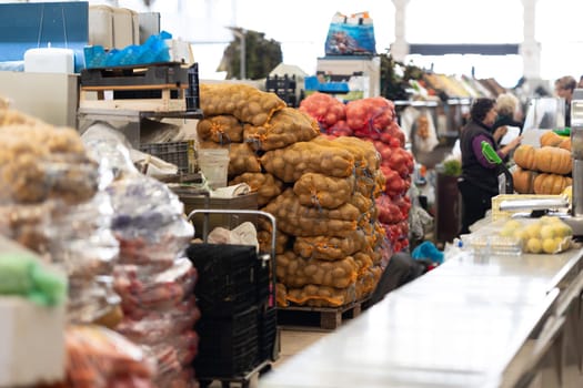 Killograms of potatoes and onions in mesh bags at the market behind the seller. Mid shot