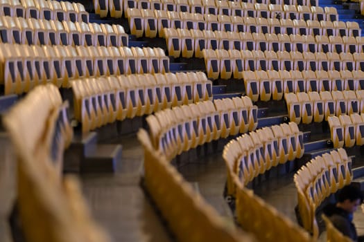 Rows of yellow seats of a rounded empty stadium. Mid shot