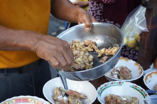 A street food vendor in Surabaya, Indonesia, is preparing a hearty soup with beef ribs and other ingredients. He's using a large metal bowl to mix the ingredients before serving them in smaller bowls.