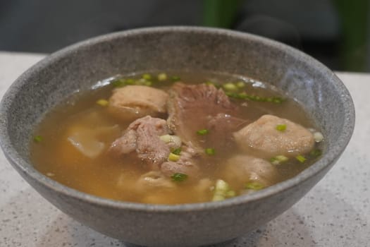 A bowl of savory bakso soup with meatballs, noodles, and broth, served with a small plate of lime wedges and chili sauce, accompanied by a bowl of vermicelli noodles and a small plate of fried shallots.