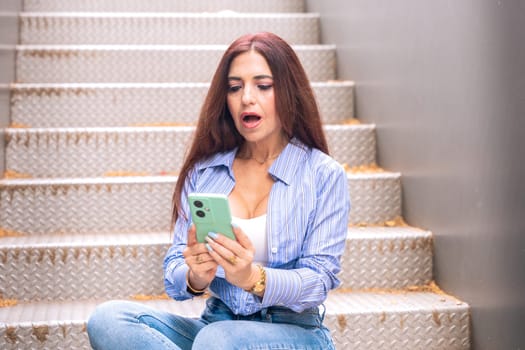 Woman sitting on stairs with cell phone in hands, writing messages and reading news online, using an app