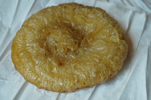 A crispy, golden-brown kue cucur, a traditional Indonesian snack made from rice flour and coconut milk, resting on a white paper napkin