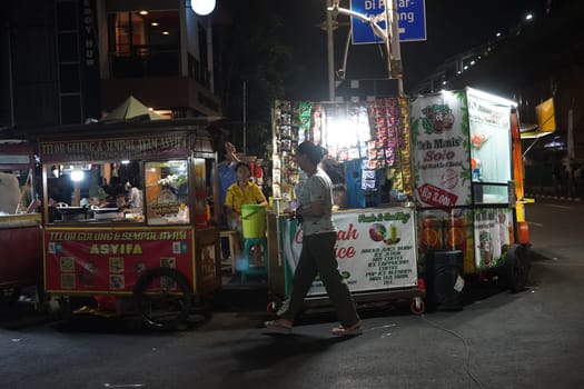 August 14, 2024. Jakarta, Indonesia. A bustling night scene in a corner of the city, filled with street vendors and shoppers.