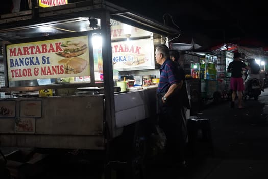 August 14, 2024. Jakarta, Indonesia. A bustling night scene in a corner of the city, filled with street vendors and shoppers.