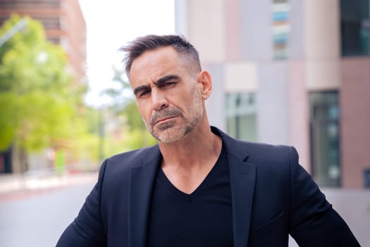 Close-up of a caucasian businessman looking angry at the camera in a suit standing in outdoor workspace. Front view of a young lawyer with thoughtful expression staring