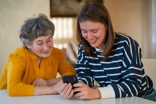 Young girl, a granddaughter, explains to an elderly relative how to use a smartphone and an application to communicate with a doctor at home. The family loves and cares for their elderly parents.