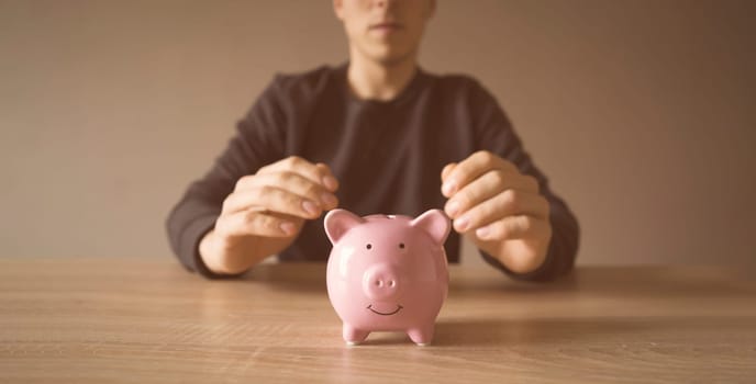 A young man is sitting at his workplace, in the foreground is a piggy bank. A businessman saves his money, takes care of the safety of his earnings, develops his business and makes investments.