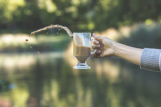 A conceptual photo of a person's hand causing a spill of the coffee from a glass mug.