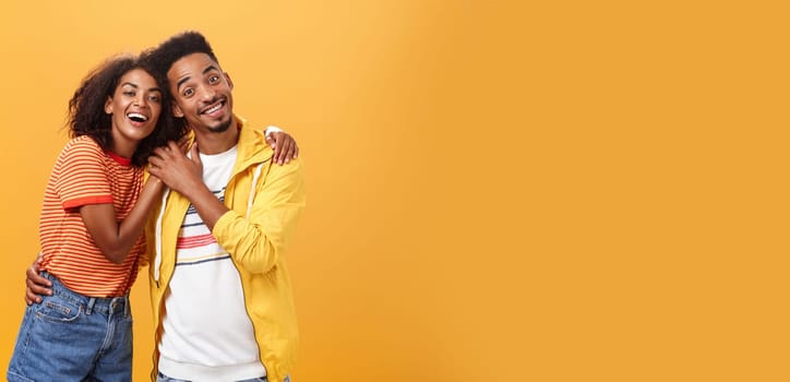 Friends always cover each other. Stylish and carefree loving african american girlfriend hugging boyfriend and smiling broadly touching guy palm hanging around and spending time great together.
