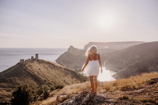 A woman stands on a hill overlooking a body of water. The sky is clear and the sun is shining brightly. The woman is enjoying the view and the peaceful atmosphere
