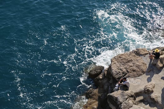 blue water sea, stone cliff, young guy tourist sunbathing, people and nature , summer day Dubrovnik, Croatia April 22, 2023. High quality photo